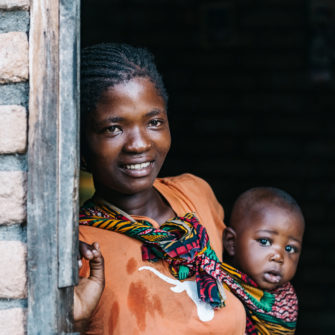 young african mother with baby looking out of the door of typical brick house