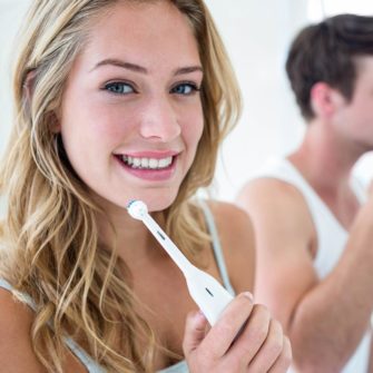 Young woman brushing teeth to maintain oral hygiene next to man