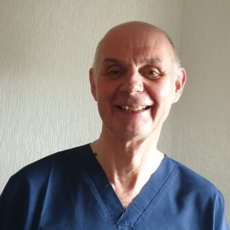 A man wearing blue medical scrubs, smiling at the camera with short hair and a light complexion.