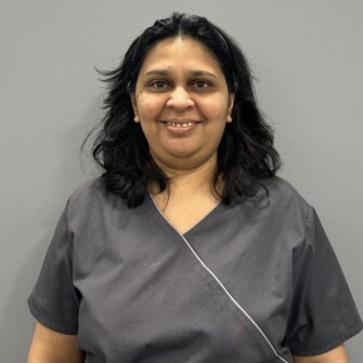 A woman wearing grey medical scrubs, standing against a plain grey background.