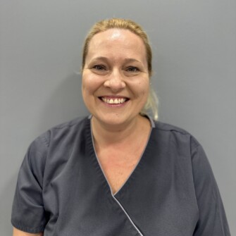 Smiling female dental professional wearing a dark grey uniform against a plain background.