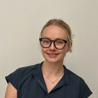 A smiling team member wearing black glasses and a navy uniform, pictured at Alloway Place Dental Care in Ayr.