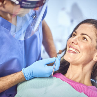 A dentist in blue scrubs examining a patient's teeth with a dental mirror during a consultation.