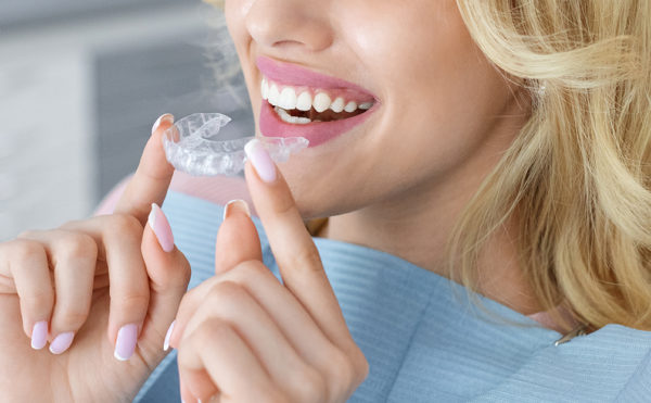 Banner for invisalign orthodontics, modern dentistry concept. Unrecognizable blonde woman with healthy white teeth holding invisible braces while sitting at dental chair, closeup portrait, copy space