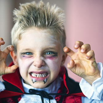 Portrait of a little boy dressed up as halloween vampire. The boy is aged 6 and is making scary face at the camera.