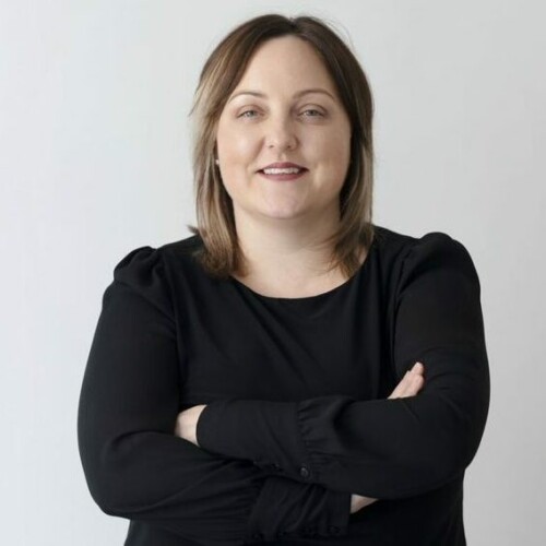 Woman standing with arms crossed, wearing a black blouse and smiling at the camera.