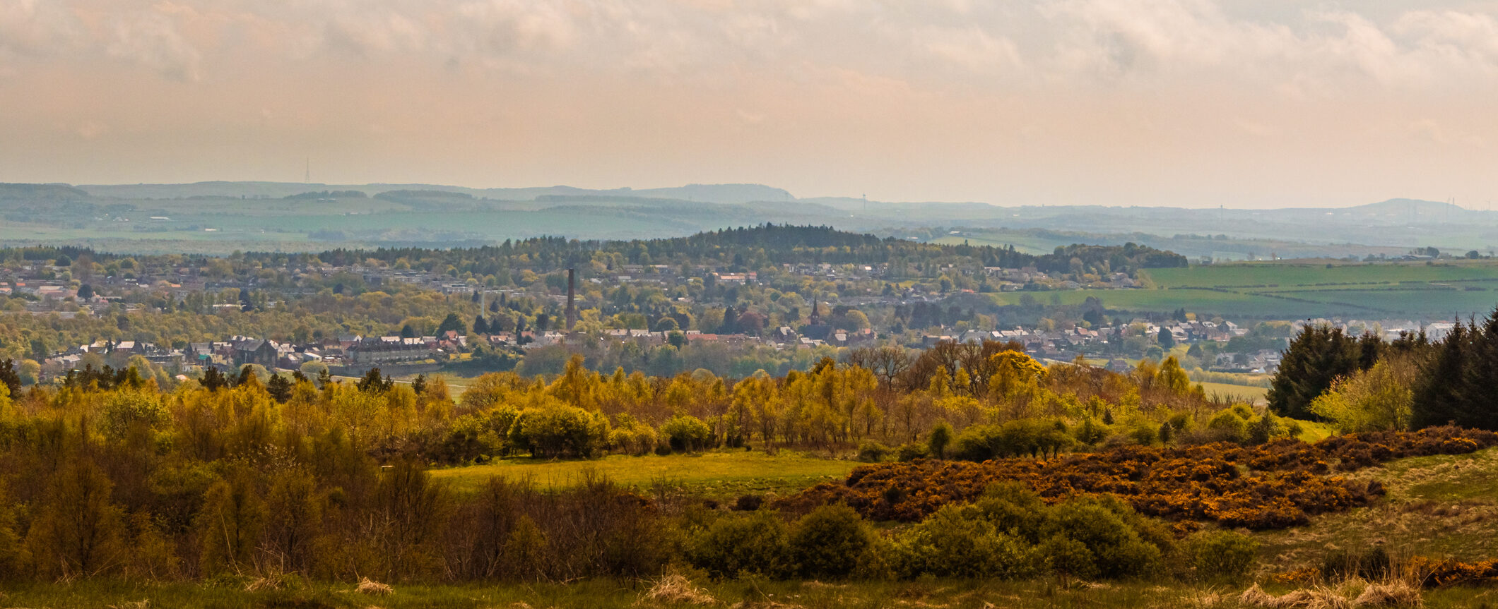 Panoramic view of Glenrothes with greenery and distant hills under a cloudy sky.