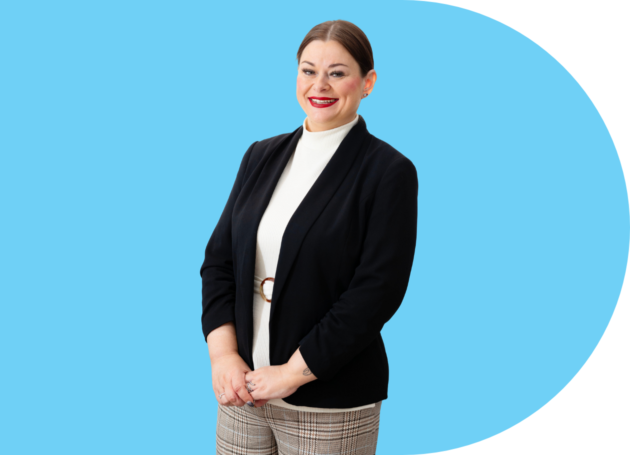 A woman wearing a black blazer and white top, standing against a blue background with a confident smile.