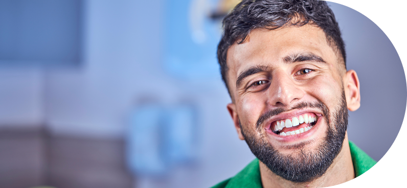 Man with a beard smiling broadly, wearing a green shirt in a dental setting.