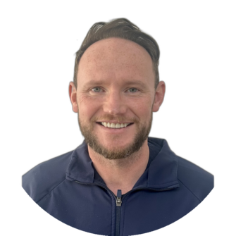 Portrait of Alan Howie wearing a navy blue zip-up jacket, smiling with short light brown hair and a beard, against a white background