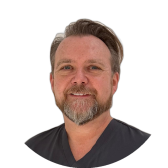 Portrait of Callum Graham wearing dark scrubs, with neatly styled hair and a trimmed beard, against a white studio background for Clyde Munro Dental