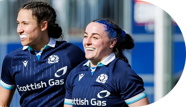 Two athletic women in navy rugby jerseys featuring the Scottish Gas sponsor, smiling during training, blue accents and curved overlay