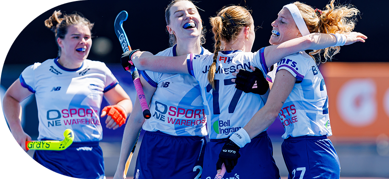 Group of female field hockey players in blue and white uniforms celebrate on the pitch, holding sticks and embracing after a match.