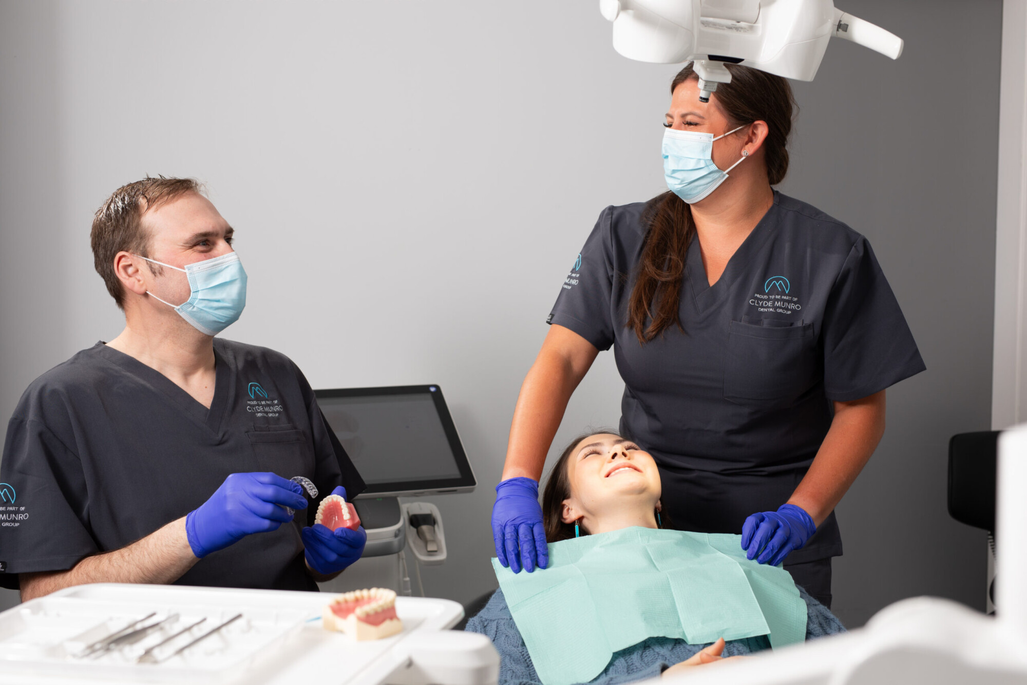 A masked Clyde Munro dental team talks with a teenage patient during an orthodontic consultation in a modern surgery.