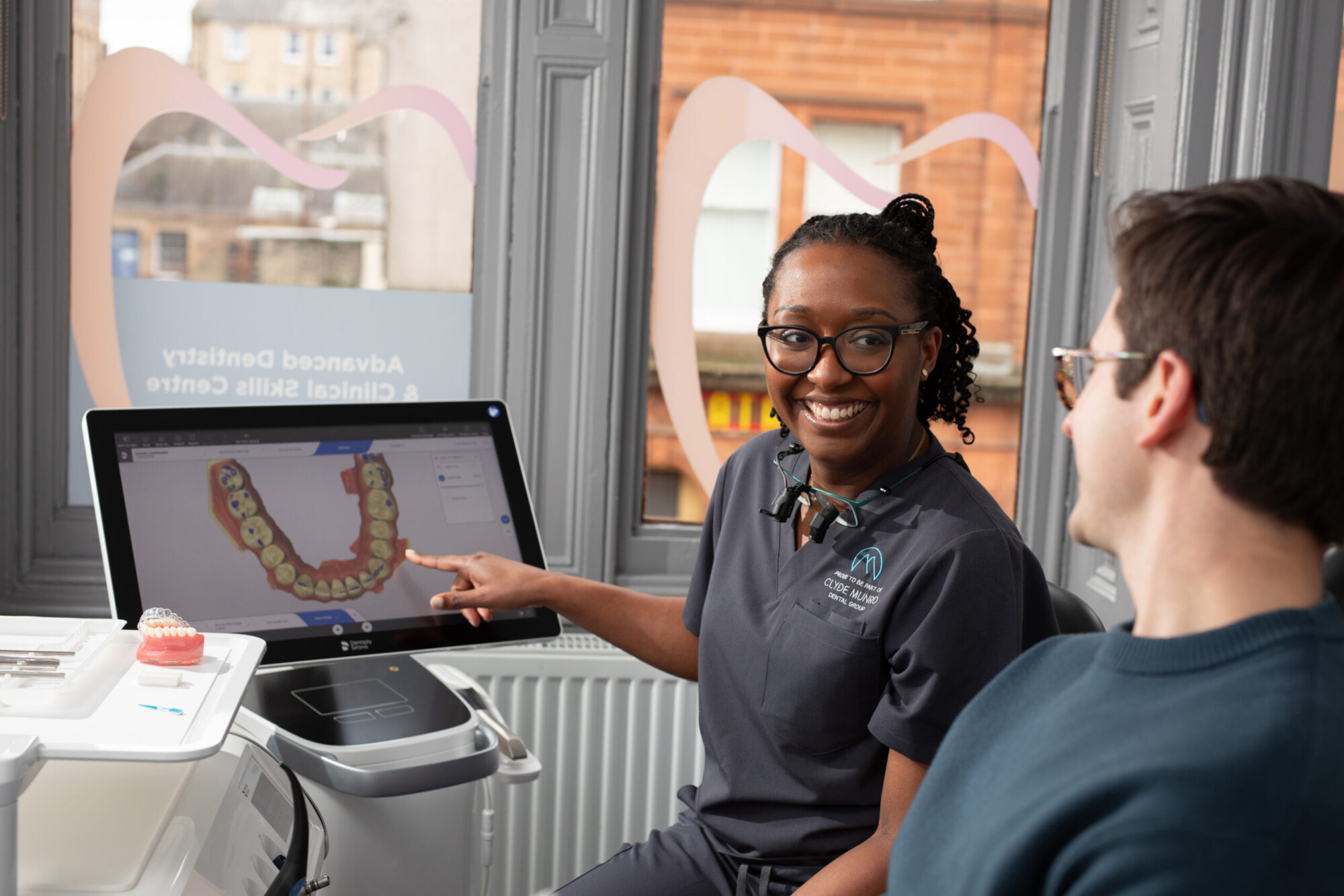 A Clyde Munro clinician points to a digital teeth scan while speaking with a patient during a fixed braces consultation.