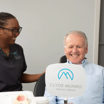 A smiling patient sits beside a dental clinician in a Clyde Munro practice during his denture fitting journey.