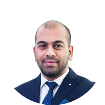 Noland Naidoo wears a navy suit, white shirt and patterned tie, with a closely shaved head and a calm expression.